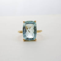 Front view of an 18ct yellow gold solitaire ring featuring a large rectangular faceted light blue aquamarine gemstone held by four claws.